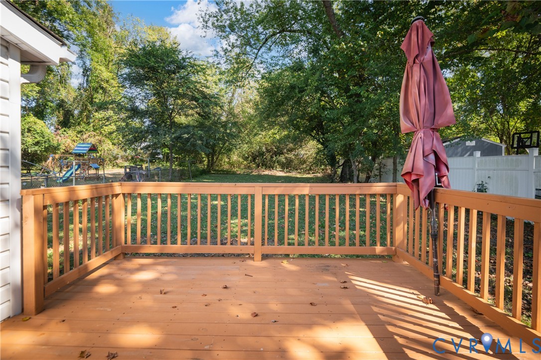 Raised wood deck featuring a railing and a spacious backyard with mature trees and perimeter fencing