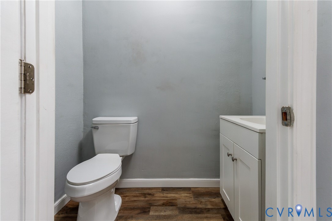 White vanity with an integrated countertop sink, wood-finish flooring, and a standard two-piece toilet