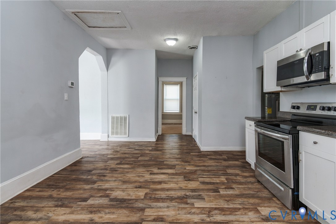 Kitchen featuring white cabinetry, dark countertops, and stainless steel appliances, including an over-the-range microwave and range, with wood-finish flooring