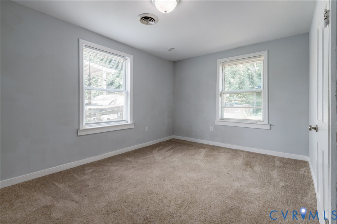 Neutral wall paint, carpeting, two windows with white trim, and a classic four-panel interior door