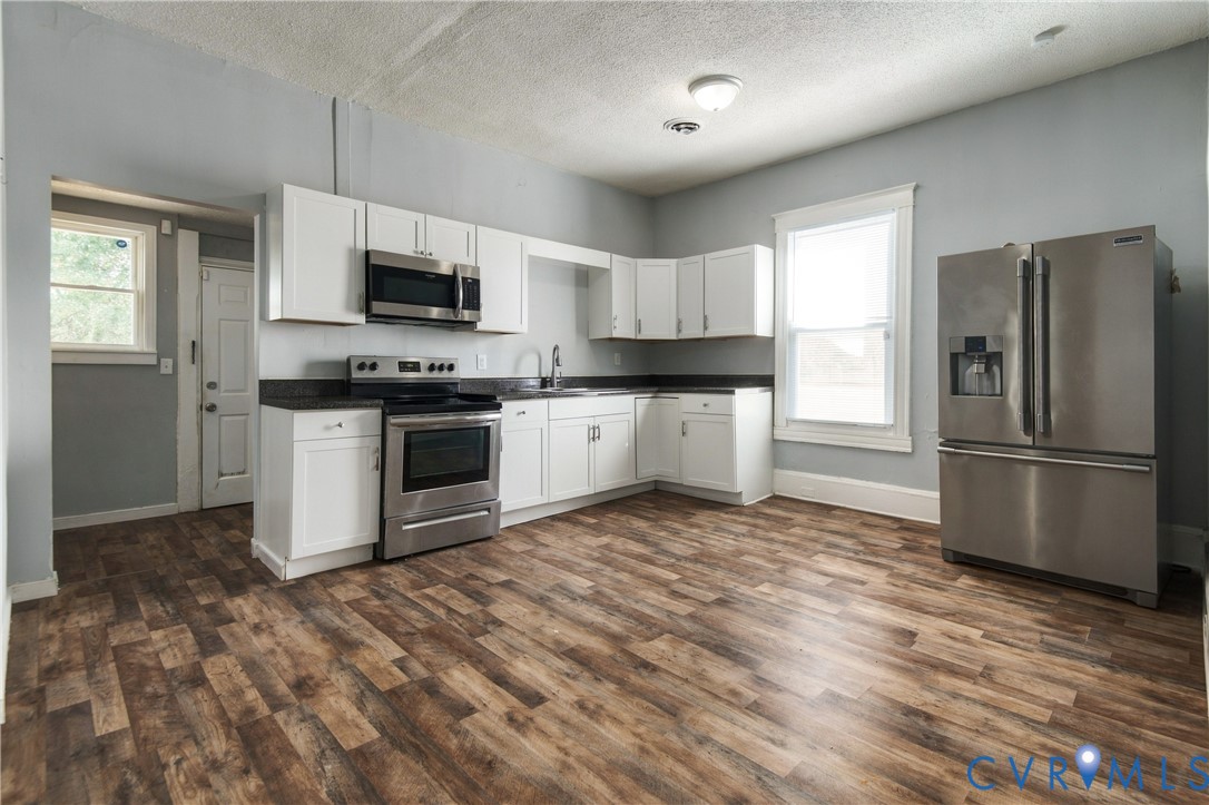 Kitchen featuring white shaker-style cabinetry, dark stone-finish countertops, stainless steel appliances, and wood-finish flooring