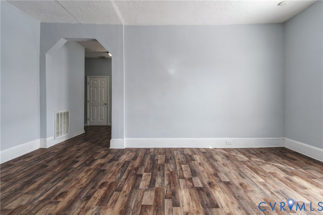 Interior space featuring wood-finish flooring, neutral wall paint, and a decorative arched doorway
