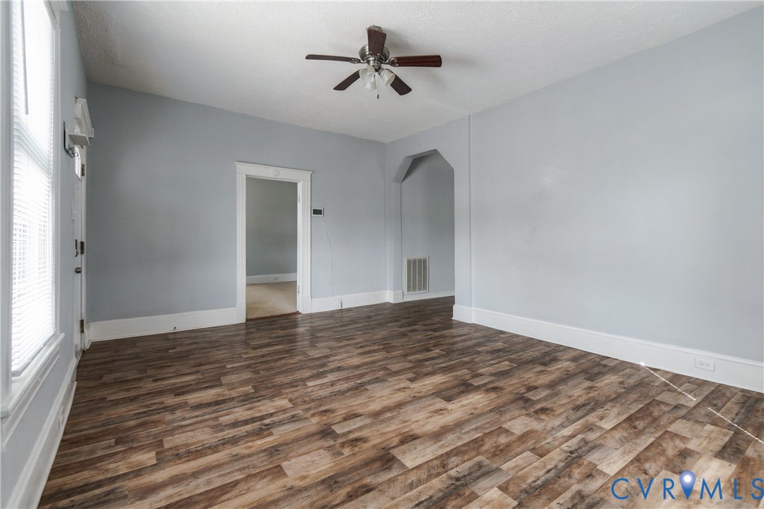 Room featuring wood-finish flooring, an arched entryway, and a ceiling fan with integrated lighting