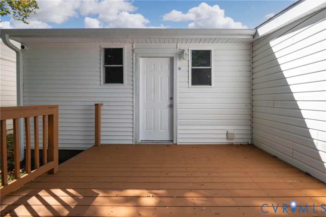 Exterior deck with horizontal wood-finish planks, white horizontal siding, two single-hung windows, and a panel entry door