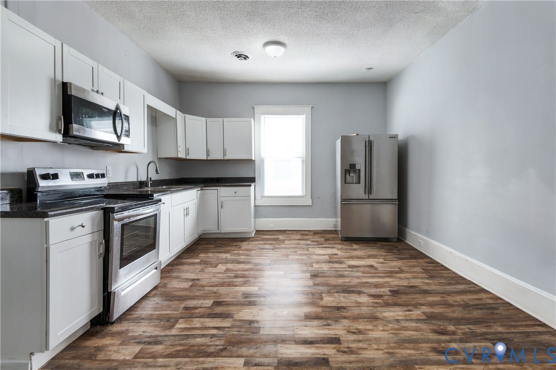 Kitchen featuring white shaker-style cabinetry, dark stone-finish countertops, stainless steel appliances, wood-finish flooring, and a single window