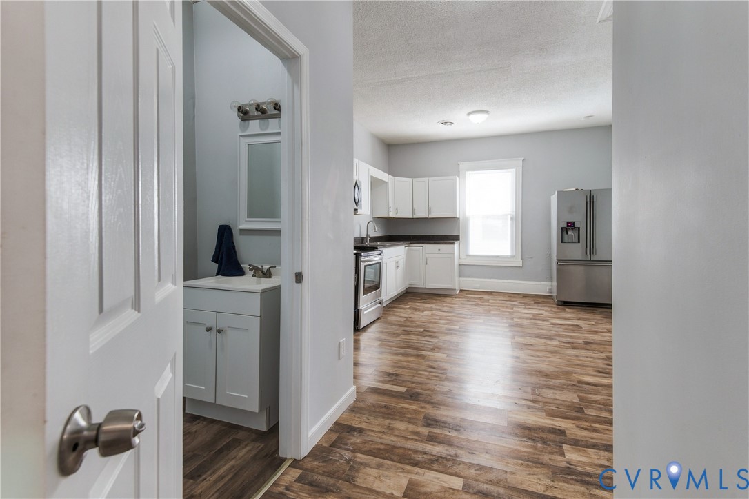 Kitchen featuring white shaker-style cabinetry, stainless steel appliances, and wood-finish flooring, with a separate vanity area containing a white cabinet and framed mirror