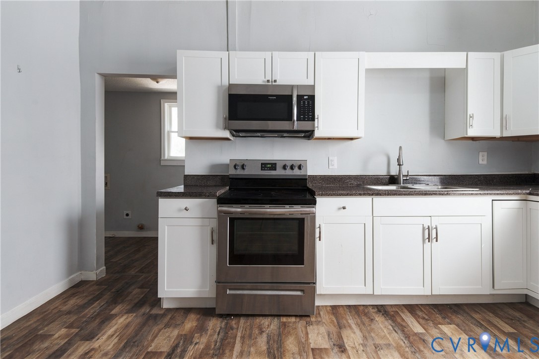 Kitchen featuring white cabinetry, dark stone-finish countertops, stainless steel appliances, and wood-finish flooring
