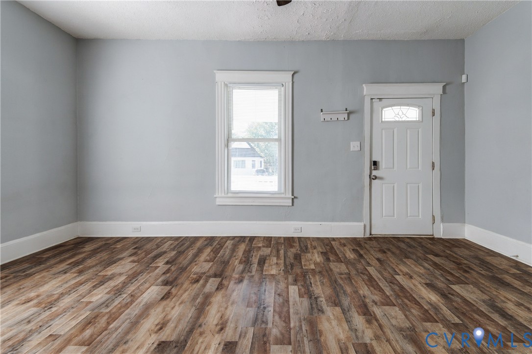 Interior space featuring wood-finish flooring, neutral wall tones, a single-hung window with decorative millwork casing, and a six-panel exterior door with a decorative glass insert