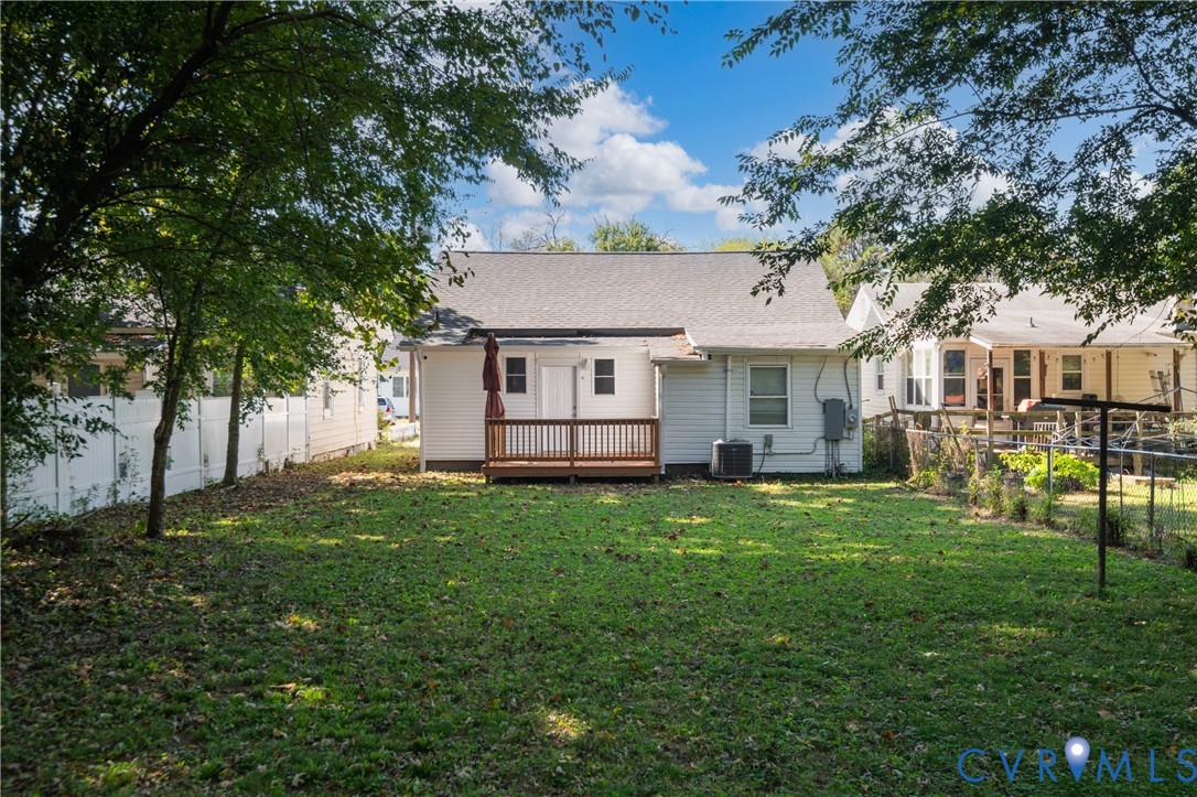 Backyard featuring a wood-decked patio, white vinyl fencing, grass lawn, and mature trees