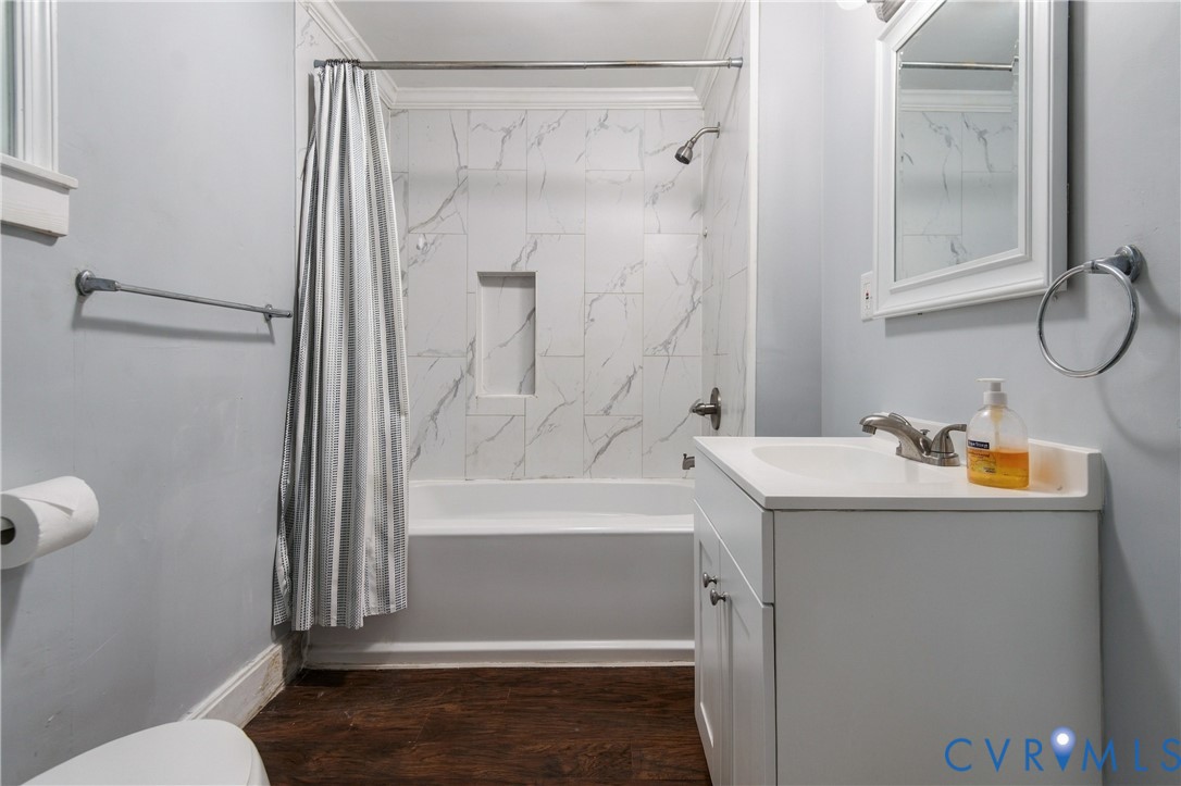 Bathroom featuring wood-finish flooring, a white vanity with an integrated countertop, tub-shower combination with full-height stone-patterned wall tile, and a built-in recessed shower niche