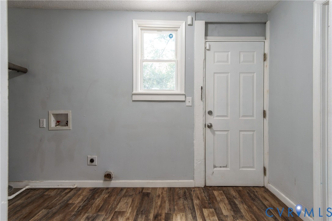 Utility area featuring wood-finish flooring, a single-hung window, white six-panel exterior door, and built-in wall-recessed plumbing connections