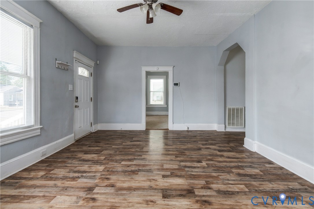 Interior space featuring wood-finish flooring, white door and window trim, an arched architectural opening, and a ceiling fan with integrated lighting
