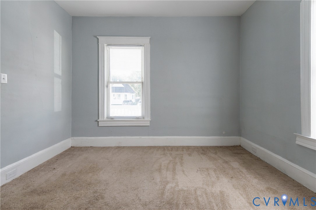 Neutral-toned interior space featuring light grey wall paint, plush carpeting, dual double-hung windows, and white window casing