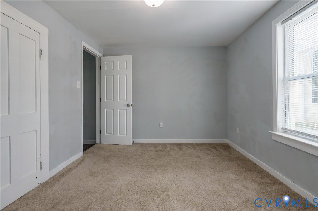 Interior space featuring neutral-tone carpeting, light grey wall finish, six-panel interior doors, and a double-hung window with fixed blinds