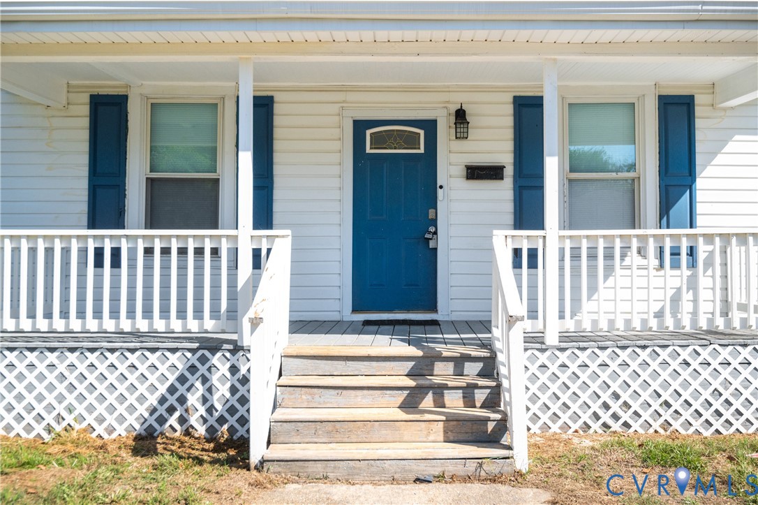 Covered front porch featuring white railings and lattice skirting, horizontal lap siding, blue shutters, and a solid front door with a decorative glass transom
