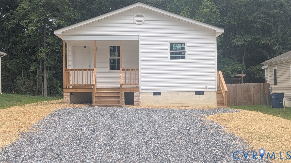 Single-story exterior featuring white vinyl siding, a covered front porch with wooden railings, and a gravel driveway