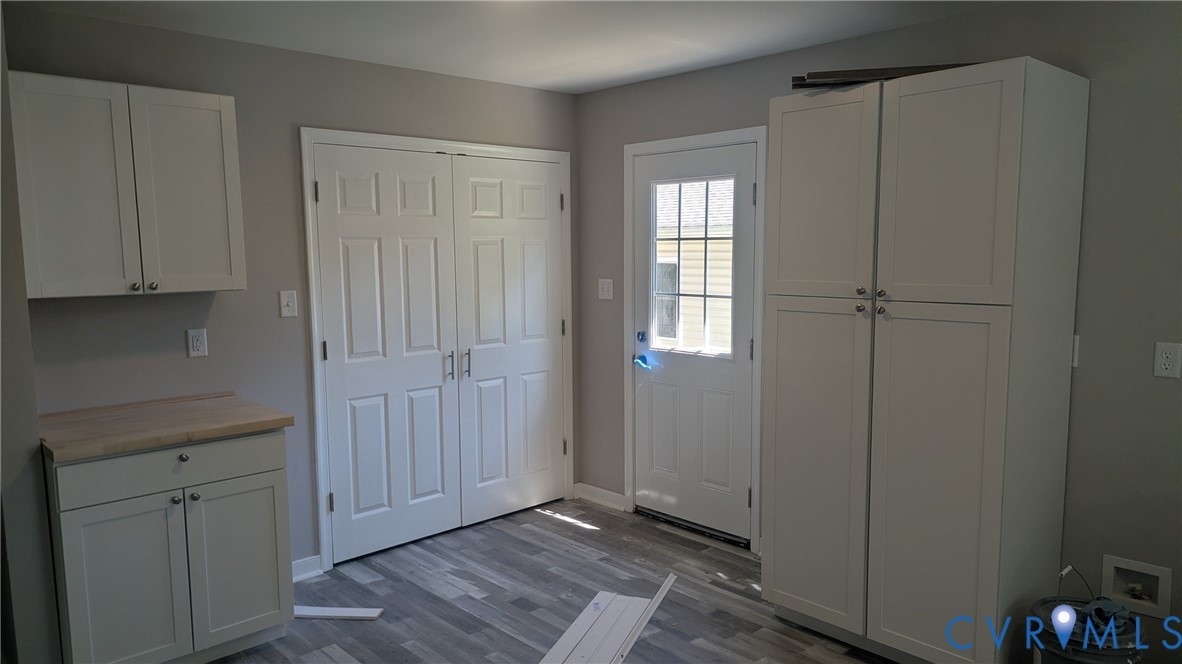 Shaker-style cabinetry, wood-finish countertop, full-height storage pantry, wood-finish flooring, and a glass-paneled exterior door