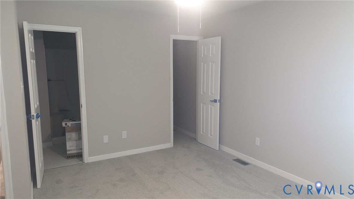 Neutral-toned interior room featuring plush wall-to-wall carpeting, crisp white six-panel doors, and a ceiling-mounted light fixture