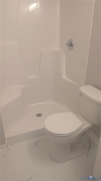 Bathroom featuring a white molded acrylic shower surround with a built-in seat, chrome shower fixture, and a white porcelain toilet on tile flooring
