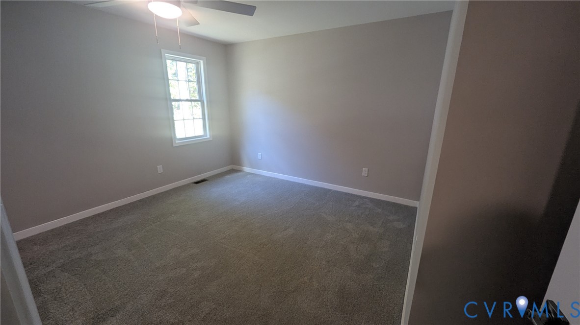 Neutral-toned interior featuring wall-to-wall carpeting, a multi-pane window, and a ceiling-mounted light fixture with a fan