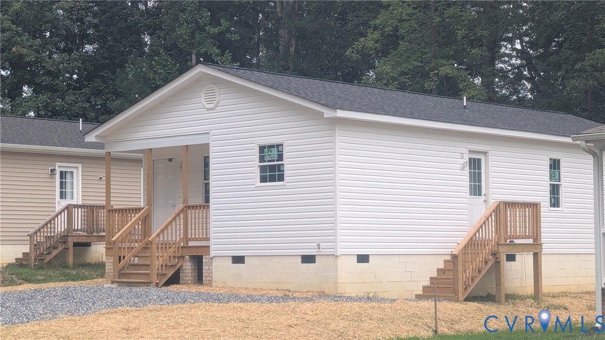 Exterior featuring white vinyl siding, a covered front porch, wooden staircase railings, a shingled roof, and a gravel driveway