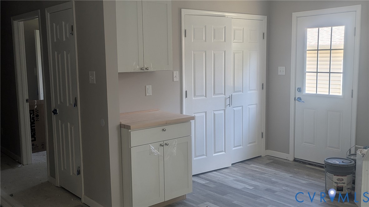 White shaker-style cabinetry, wood-finish countertop, wood-finish flooring, six-panel interior doors, and exterior door with a multi-pane glass insert