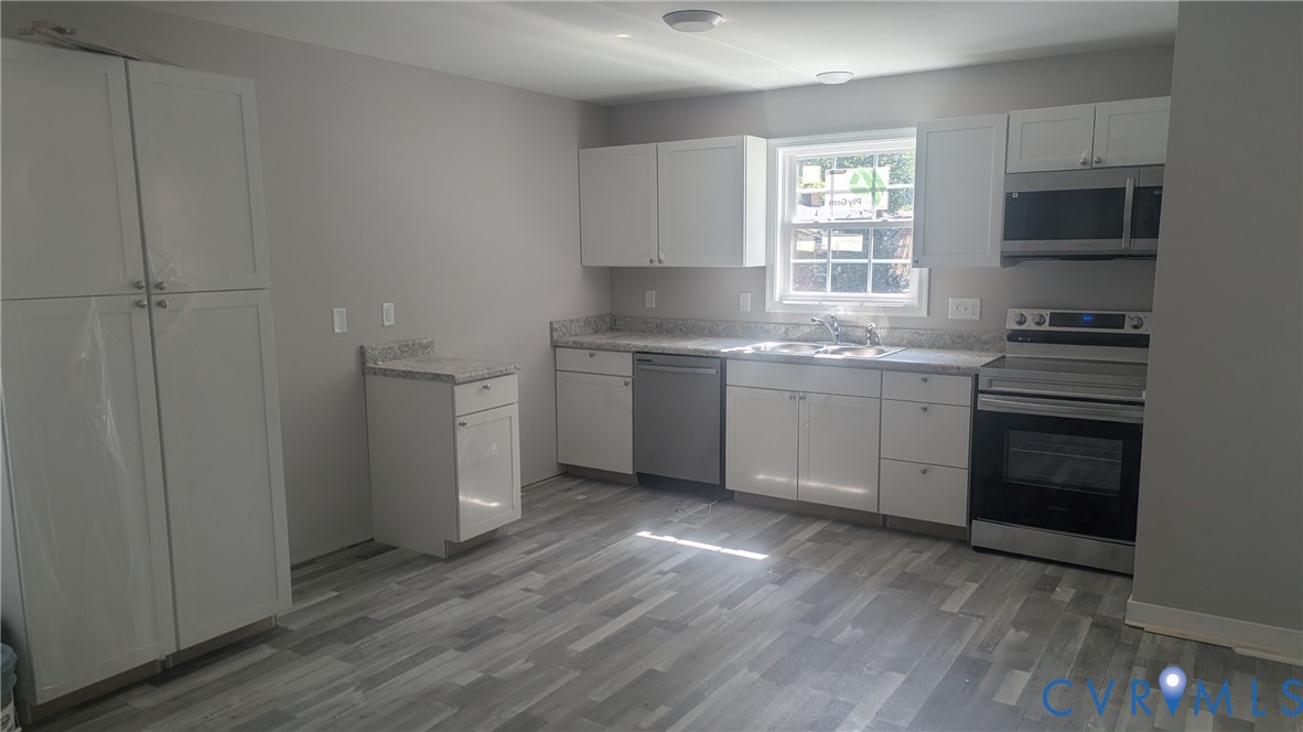 Kitchen featuring white shaker-style cabinetry, speckled stone-finish countertops, stainless steel appliances, and grey wood-finish flooring