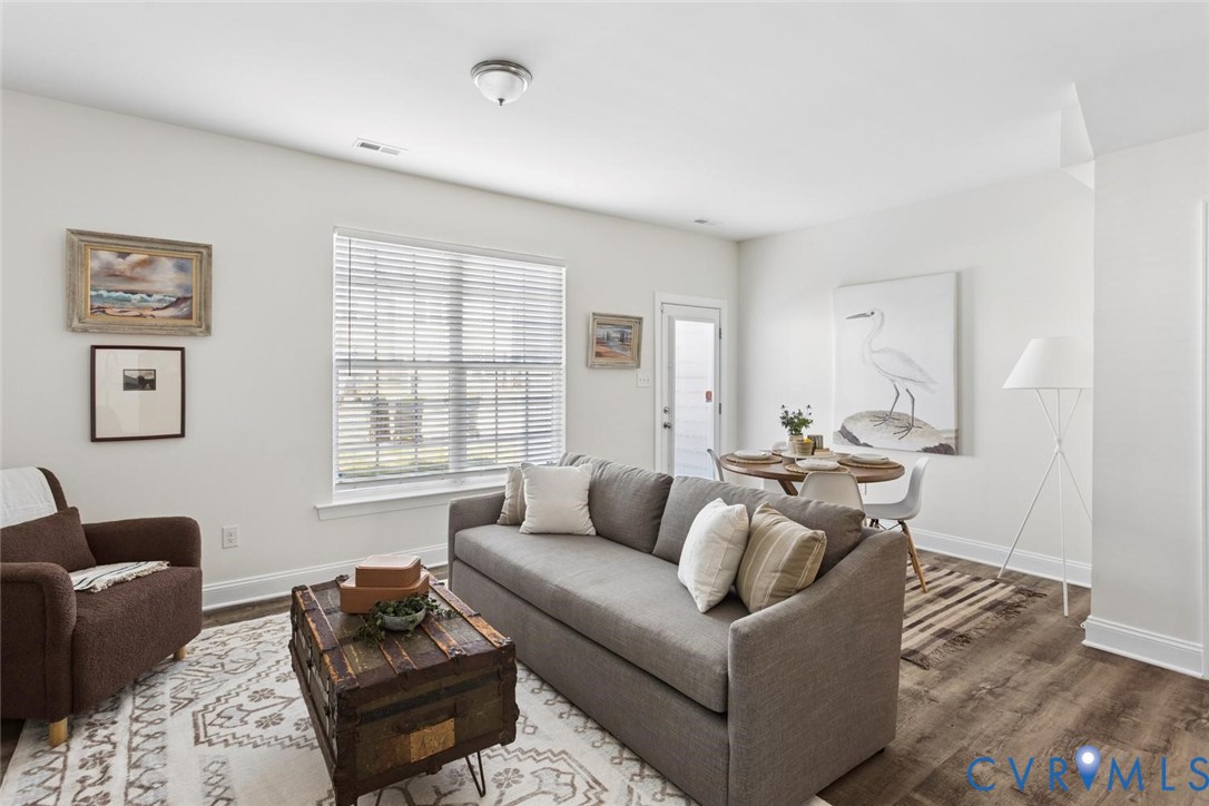 Open-concept living area featuring wood-finish flooring, white walls, and a large window with blinds.