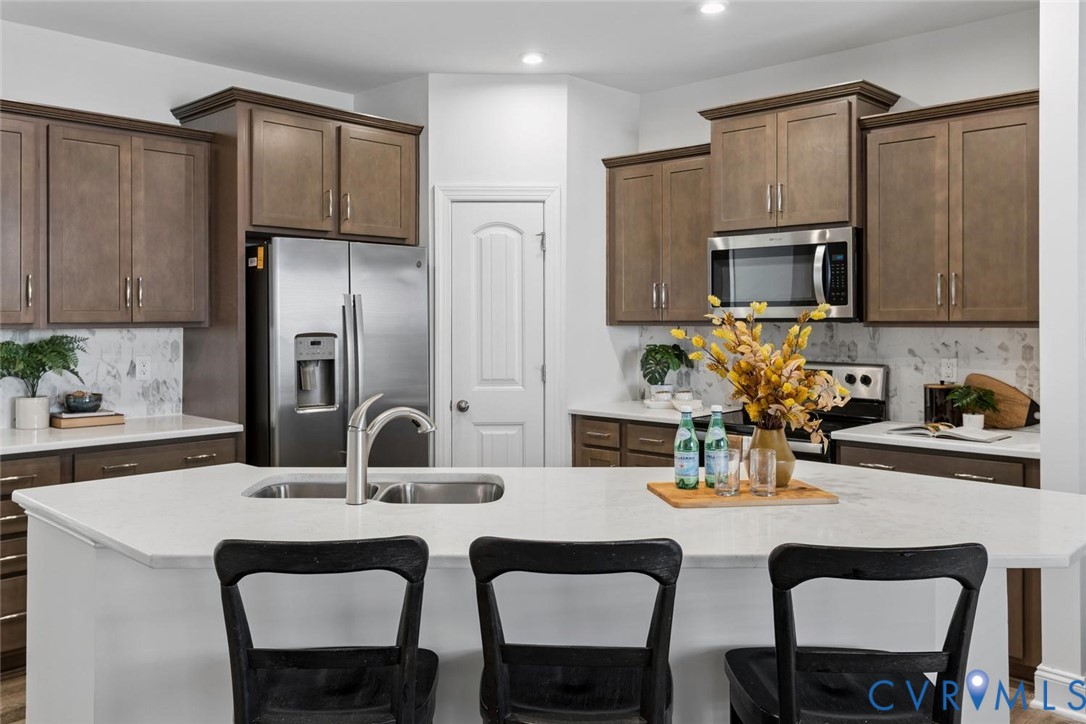 Kitchen featuring wood-finish cabinetry, stainless steel appliances, quartz island with an integrated sink, and a patterned backsplash.