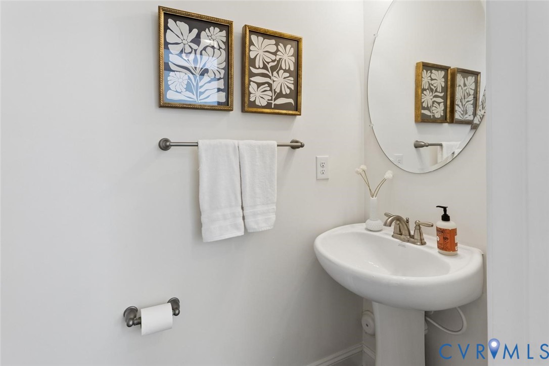 Pedestal sink with a brushed nickel faucet, wall-mounted oval mirror, and a coordinating towel bar.