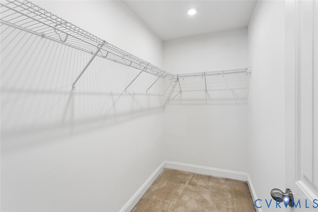 Spacious walk-in closet in your Primary Bedroom featuring wire shelving, recessed lighting, and carpet flooring.