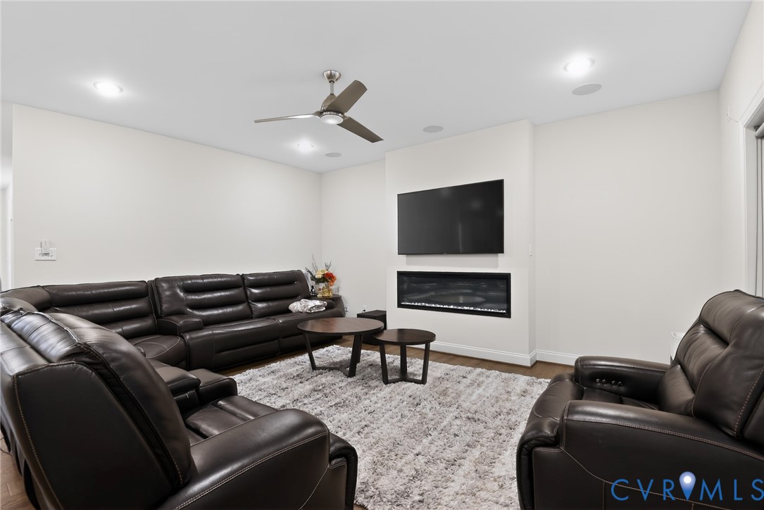Recessed ceiling lighting, linear wall-mounted electric fireplace, and multi-blade ceiling fan