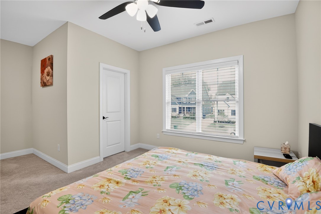 Neutral wall tones, carpeted flooring, multi-pane window with blinds, and a ceiling fan with integrated lighting