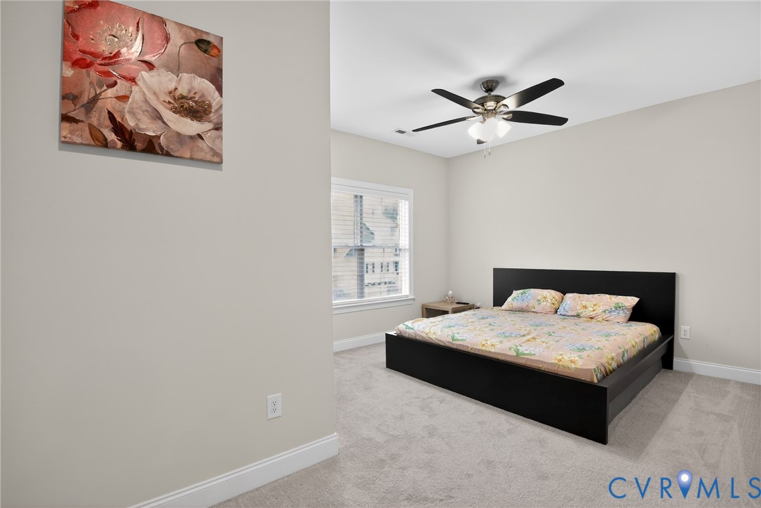 Neutral-toned interior room featuring wall-to-wall carpeting, a multi-blade ceiling fan with integrated lighting, and a window with white casing