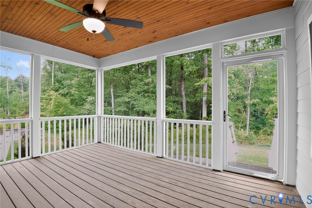 Screened porch featuring a wood-plank ceiling, composite decking, white baluster railings, and a ceiling-mounted light fixture with a fan