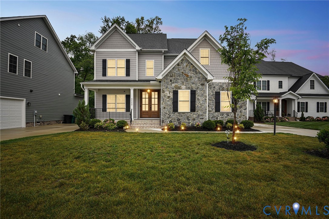 Two-story residence featuring a stone veneer and horizontal lap siding exterior, a covered front porch, decorative shutters, and a double-door entryway Two-story residence featuring a stone veneer and horizontal lap siding exterior, a covered front porch, decorative shutters, and a double-door entryway