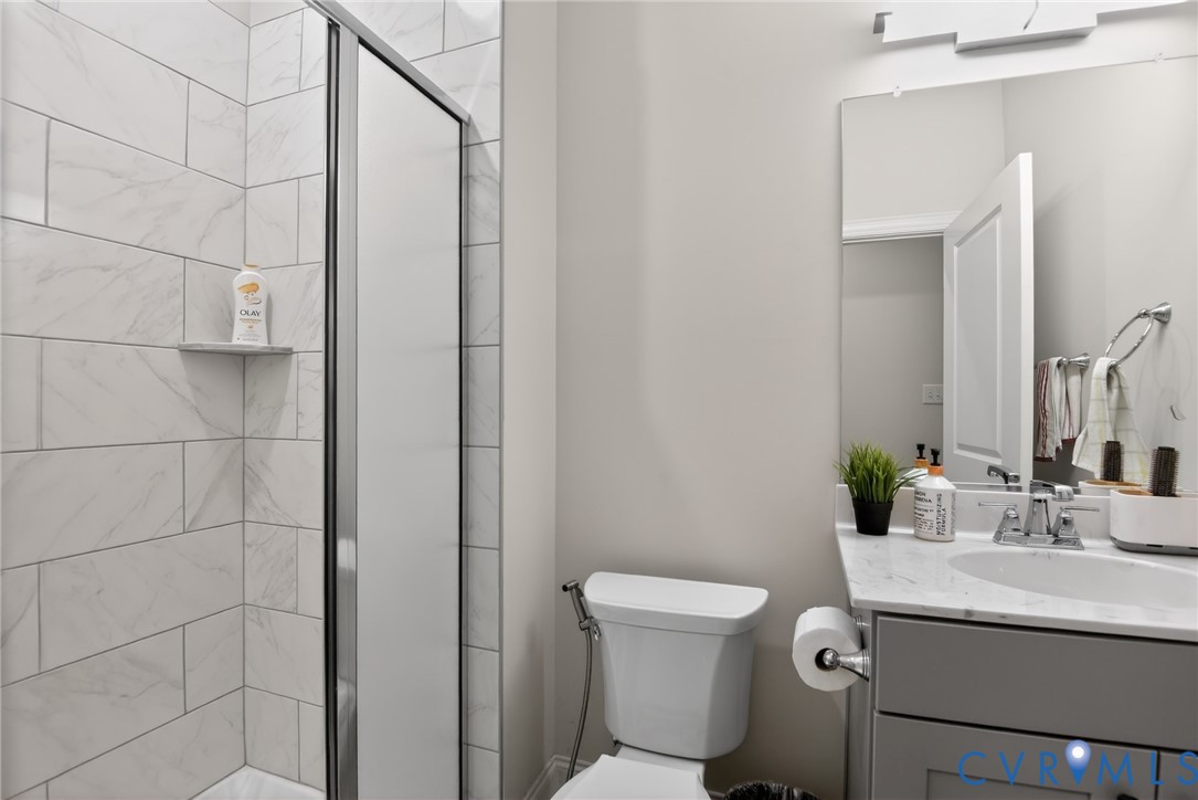 Bathroom featuring a shower with floor-to-ceiling stone-finish tile surround, a built-in shower niche, a vanity with stone-finish countertop, and a wall-mounted light fixture