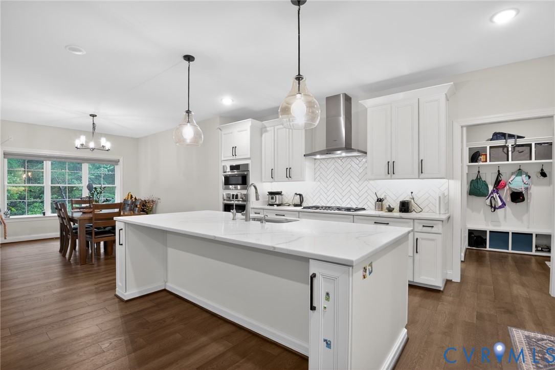 Kitchen featuring a large central island with quartz countertops, custom white cabinetry, herringbone tile backsplash, stainless steel range hood, and wood-finish flooring