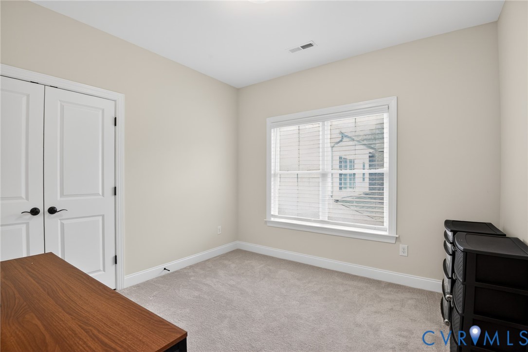 Neutral interior featuring wall-to-wall carpeting, dual-panel closet doors with matte black hardware, and a window with white casing