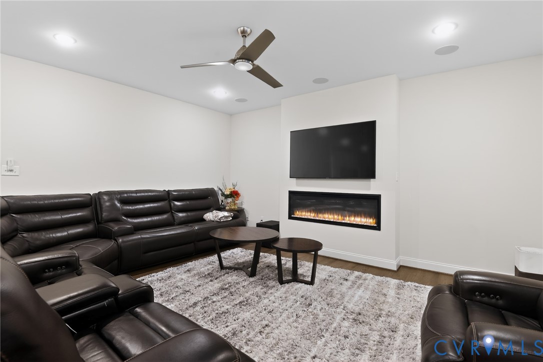 Living space featuring a linear electric fireplace, built-in television mount, recessed lighting, and a multi-blade ceiling fan