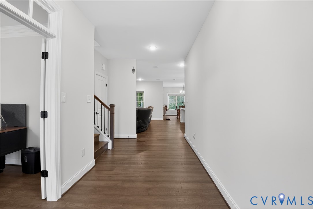 Interior hallway featuring wood-finish flooring, recessed lighting, and a staircase with a dark-stained wood handrail and square balusters