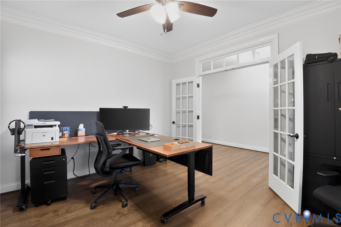 Room featuring wood-finish flooring, crown molding, double French doors with transom windows, and a ceiling fan with integrated lighting