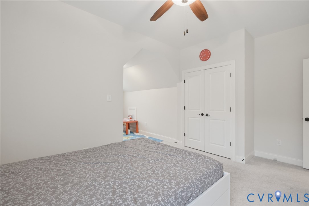 Room featuring neutral wall tones, carpeted flooring, a ceiling fan, and double-door closet storage with black hardware