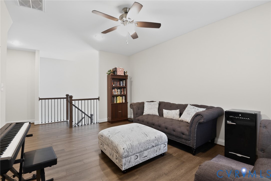 Open-concept area featuring wood-finish flooring, vaulted ceiling, and a central ceiling fan with integrated lighting, finished with a dark-stained wood baluster railing