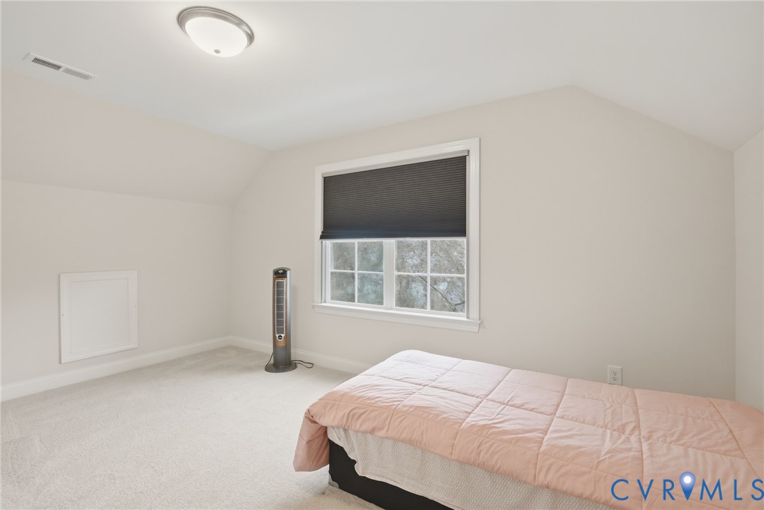 Neutral-toned room with vaulted ceilings, wall-to-wall carpeting, and a multi-pane window featuring a window shade