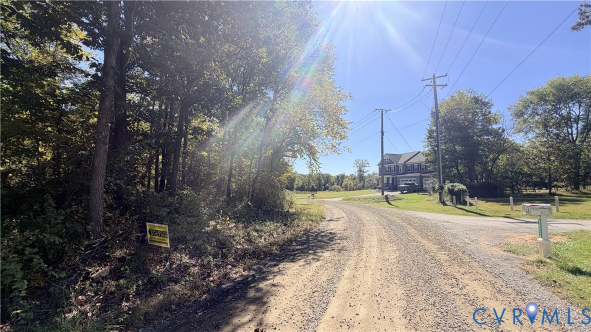 Unpaved access road bordering a wooded area featuring mature trees