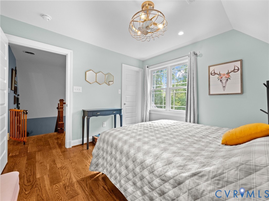 This spacious upper-level bedroom features beautiful hardwood floors, a ceiling fan, a generous walk-in closet, and large windows that fill the room with natural light while offering peaceful views of the surrounding countryside.