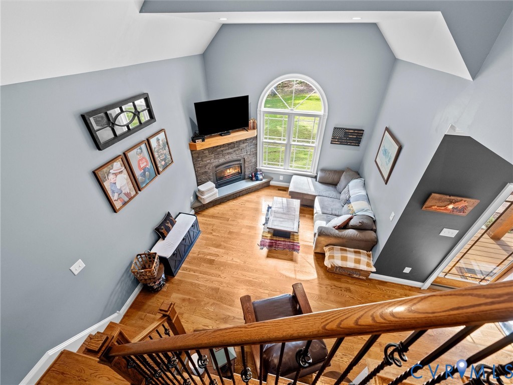 A beautiful view from the upper level overlooks the spacious two-story family room, showcasing the soaring ceilings, dramatic arched window, stacked stone gas fireplace, and gleaming hardwood floors. An open, airy design filled with natural light!