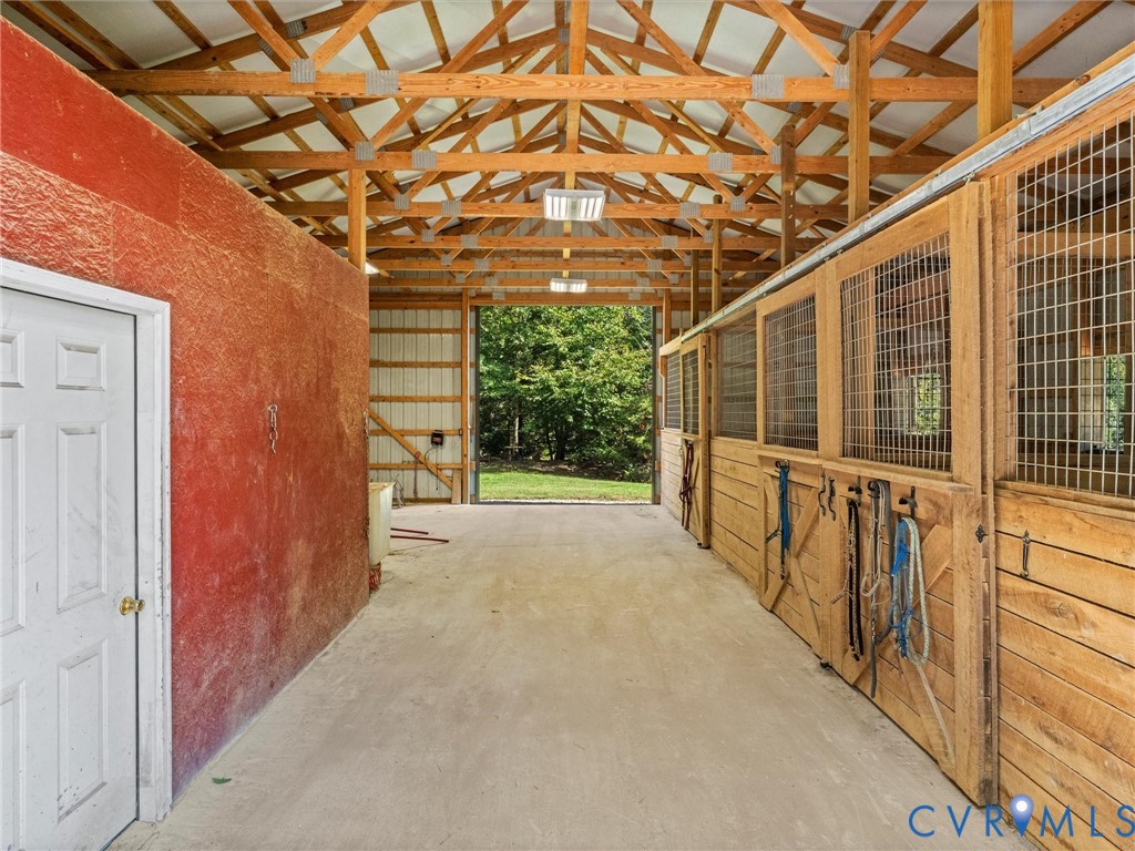 Another view of the spacious barn aisle showcases the exposed wood trusses, attractive stall fronts, and convenient tack room access. The open layout provides plenty of room for grooming, tacking up, and everyday horse care!
