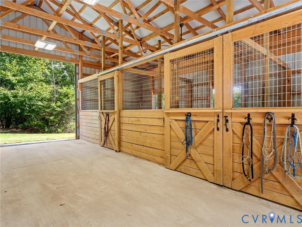 The well-designed 3-stall horse barn features spacious stalls with attractive wood fronts, sliding stall doors, and an open, airy center aisle. Exposed wood trusses and generous natural light create a bright, welcoming environment, while the convenient layout makes daily horse care a breeze!